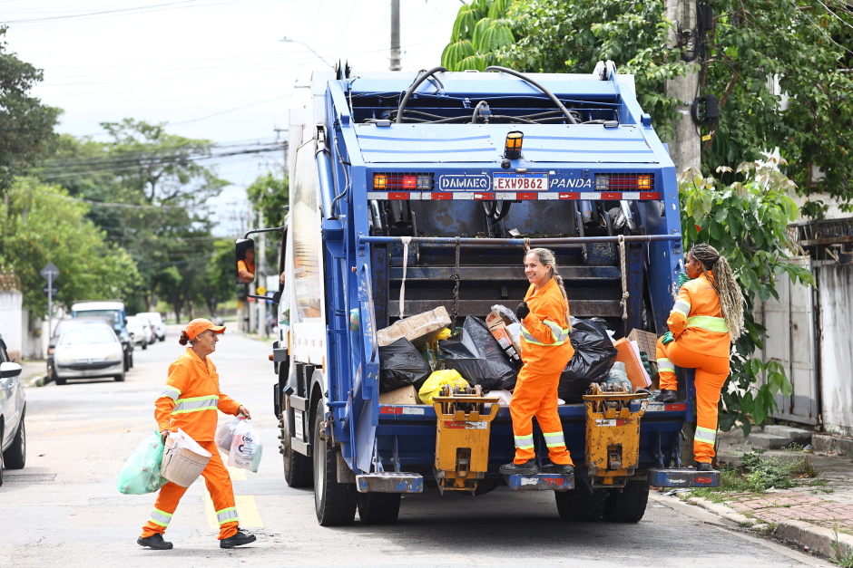 Coletoras de resíduos da Urbam trabalham sorrindo próximas ao caminhão da coleta
